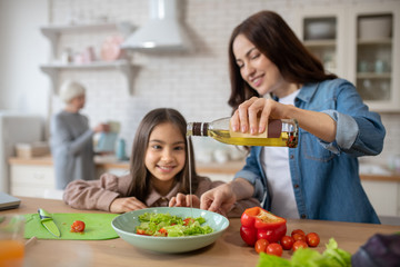 Mom with daughter seasoning vegetable salad with olive oil.