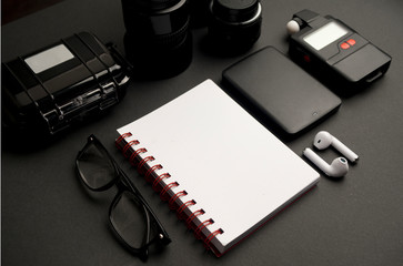 set accessories work photographer on table, white notebook, glasses, white phone, two black lenses with cover, hard disk, photometer, white headphones with white box, on black background