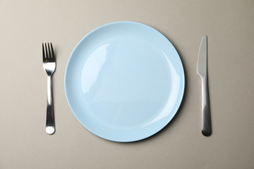 Plate, fork and knife on grey paper background, top view