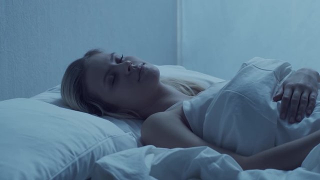 Young woman lying in the bed at night. Beautiful blond sleeping girl. Twilight in the bedroom, moonlight from the window.