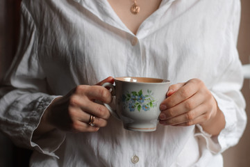 woman with  vintage cup of tea,  girl in a white blouse holds a cup in her hands, white cup with blue flowers in female hands