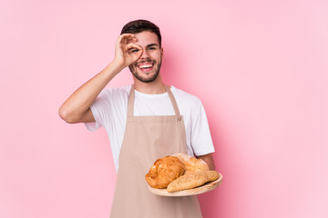 Young caucasian baker man isolated excited keeping ok gesture on eye.