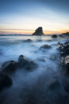 Waves crash around rocks with dramatic sea stacks in the background on a secluded beach in Sonoma Coast State Park located in between Jenner and Bodega Bay, California.