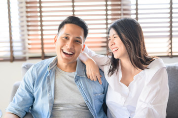 Fototapeta premium Asian couple in love smiling and laughing on sofa at home
