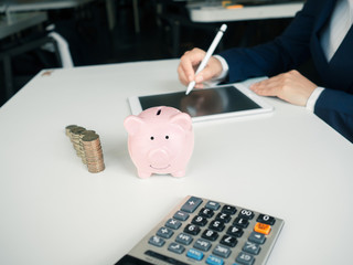 piggybank and business women working and calculate expenses with calculator and laptop. stak of...