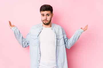 Young caucasian business man posing in a white background isolated confused and doubtful shrugging shoulders to hold a copy space.< mixto >