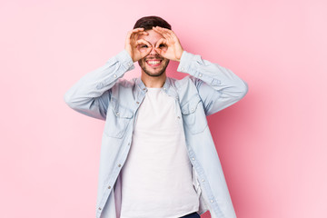 Young caucasian business man posing in a white background isolated showing okay sign over eyes< mixto >