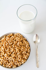 Bowl of whole grain oat cereal with a silver spoon, and a glass of milk on a white background, top view. Heart shapes cereal. 