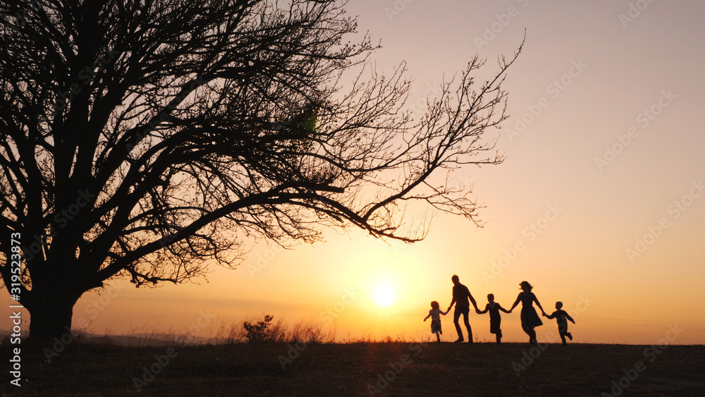 Wall mural Silhouettes of happy family walking together in the meadow during sunset