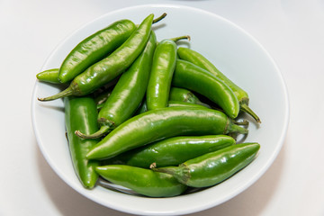 green hot peppers in a white plate over a  white background