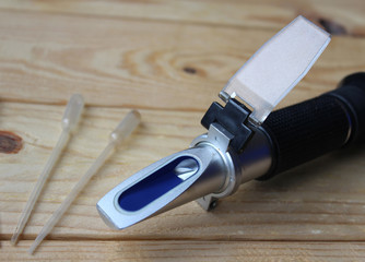 Close up image of a hand held Refractometer and pipettes on a wooden table.