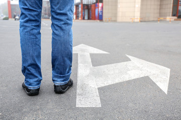 Young man standing on road with arrows marking. Concept of choice