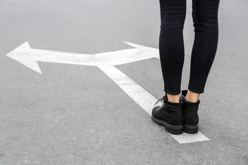 Young woman standing on road with arrows marking. Concept of choice