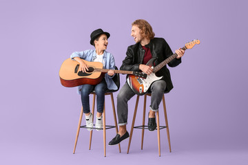 Man and his little son playing guitars on color background