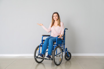 Handicapped young woman in wheelchair near light wall
