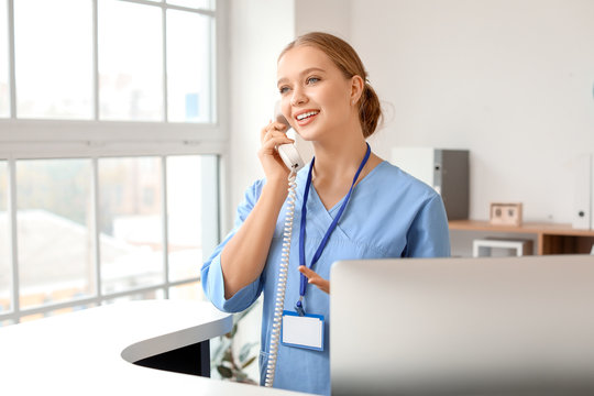 Young female receptionist talking by telephone at desk in clinic