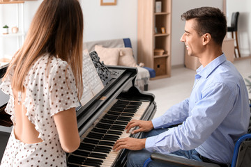 Woman teaching young man in wheelchair to play piano