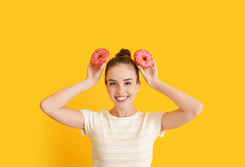 Funny young woman with tasty donuts on color background