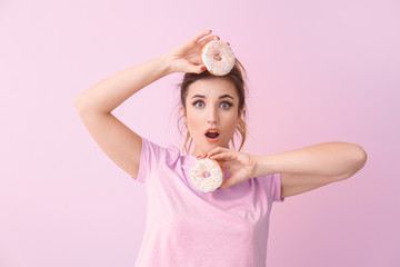 Obraz na płótnie Canvas Surprised young woman with donuts on color background