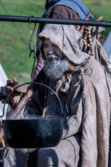 Middle-aged, bearded and ragged beggar, wandering a camp, looking for food