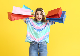 Stressed female stylist with shopping bags on color background