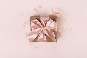 Gift box wrapped in craft paper with perfect pink ribbon on pale pink rustic background.