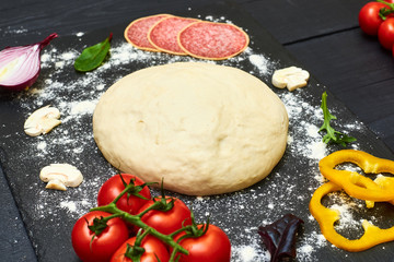 Pizza dough with ingredients on a dark background.
