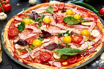 Raw pizza with mozzarella cheese, meat, tomatoes, mushrooms, peppers, herbs on a dark wooden background. Cooking delicious italian pizza.