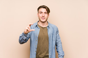 Young caucasian man posing isolated holding something little with forefingers, smiling and confident.