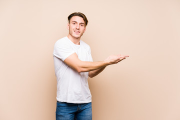 Young caucasian man posing isolated holding a copy space on a palm.