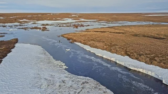 skilled canoeist sails along narrow raging river opening with ice pieces and turns around near brown meadows aerial view