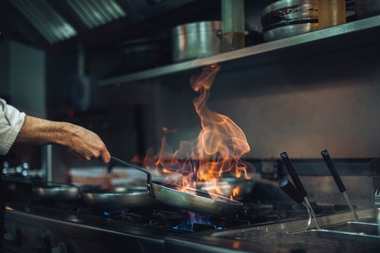 Chef preparing a flambe dish at gas stove in restaurant kitchen