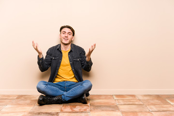 Young caucasian man sitting on the floor isolated joyful laughing a lot. Happiness concept.