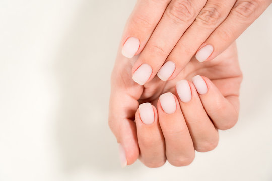 Closeup top view of 2 beautiful hands of woman with professional manicure, nails painted with light pink color and covered with mat top without glossy shine. Nude style design of fingernails.