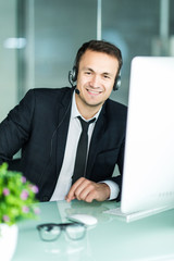 Handsome businessman in suit and headset is smiling while working with laptop in office