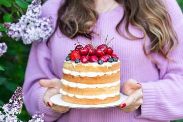 Homemade summer biscuit cake with cream and fresh berries in woman hands In the garden Lilac Soft focus