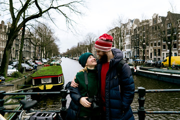 Loving couple man and woman having fun on the streets of Amsterdam in winter warm clothes. Husband embracing wife. Funny moments of life together. Valentine day concept