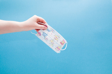  hand holds children's medical protective mask with drawings on a blue background copy space, hand...