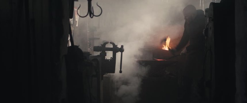 Blacksmith hammering molten iron on anvil dark eerie smoke cinemascope widescreen