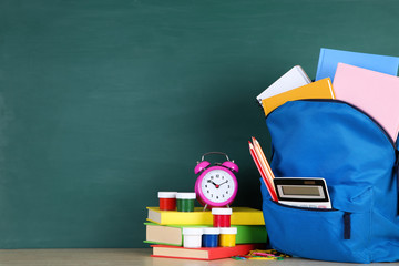 School supplies with blue backpack on blackboard background