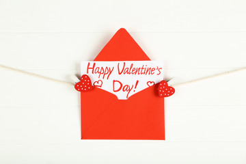 Paper envelope with text Happy Valentines Day hanging on white wooden background