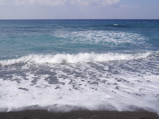 Naklejka na ściany i meble Seascape on the island of Santorini, Greece. Sea waves with foam on a sunny day.