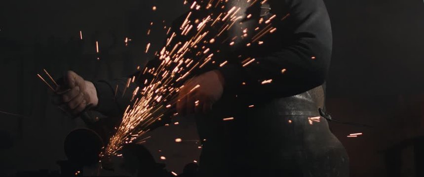 Blacksmith with angle grinder sparks unrecognisable dark close up cinemascope widescreen