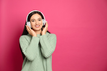 Young woman listening to audiobook on pink background. Space for text