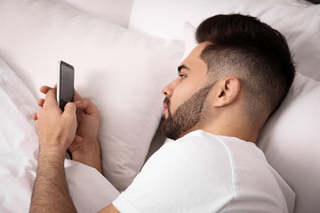 Young man addicted to smartphone in bed at home