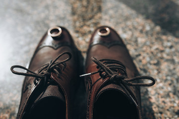 Tied shoelaces, wedding gold rings on brown leather shoes of the groom close-up. Photography, concept, top view.