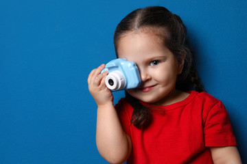 Fototapeta premium Little photographer taking picture with toy camera on blue background