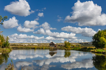 Fototapeta na wymiar Photo of a lonely wooden house on the lake, which reflects summer clouds against the backdrop of chalk hills