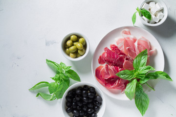 Set of jamon Iberico and Serrano on a white plate with olives, cheese and basil. Antipasti snack
