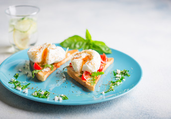 Two poached eggs on toasted toast with cherry tomatoes, cheese and herbs on a large blue plate